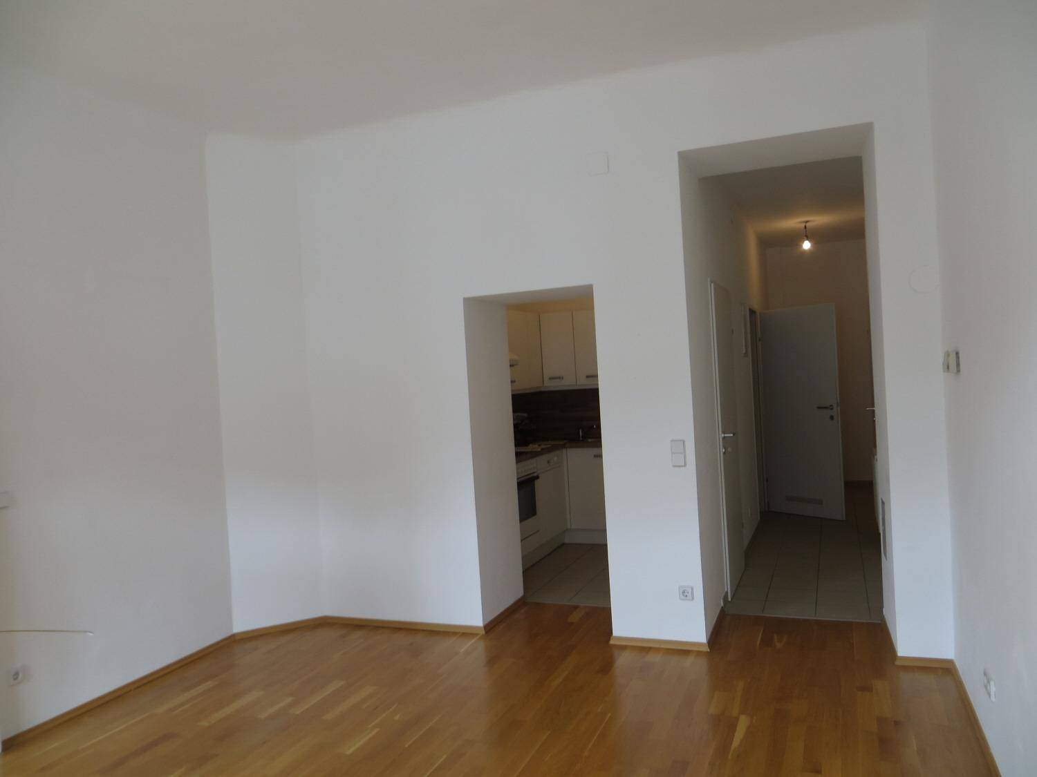 Geräumiges Zimmer mit Parkettboden und Durchgang zur Küche sowie zum Flur.