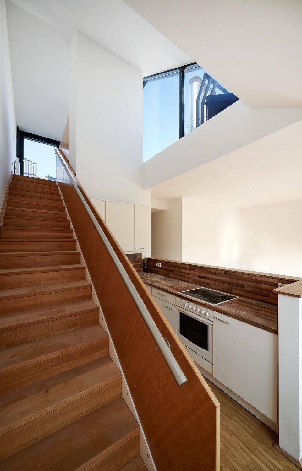 Offener Wohnbereich mit integrierter Küche, Holztreppe und viel Tageslicht.