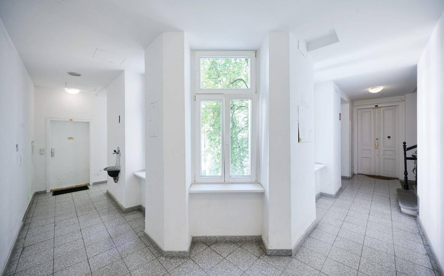 Heller Flur mit Fenster und Fliesenboden, der zu verschiedenen Wohnungen führt.