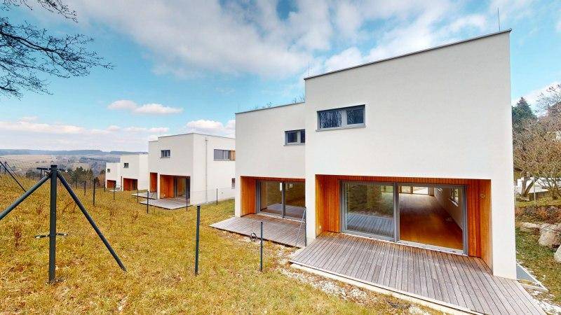 Rückseite moderner Häuser mit Holzterrassen und Blick auf die hügelige Landschaft.