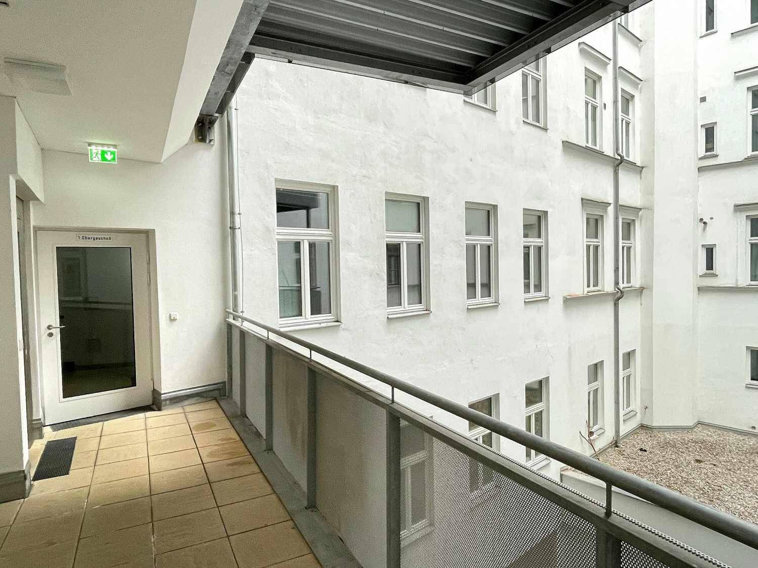 Heller Flur mit Fliesenboden und einem Fenster, das den Blick auf einen ruhigen Innenhof freigibt.