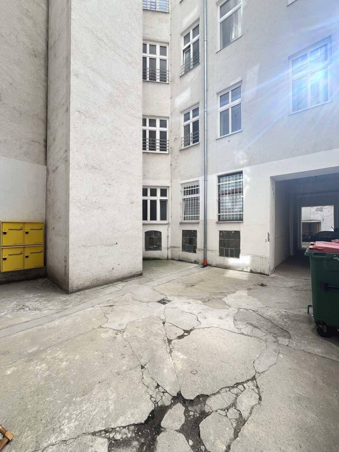 Heller Innenhof mit Betonboden, Briefkästen und einem Durchgang zu weiteren Gebäudeteilen.