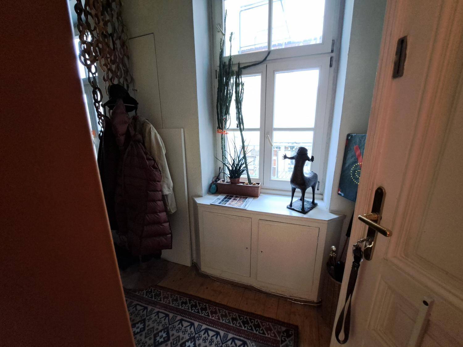 Heller Flurbereich mit Fenster, Holzboden und einer kleinen Kommode unter dem Fenster, einladend gestaltet.