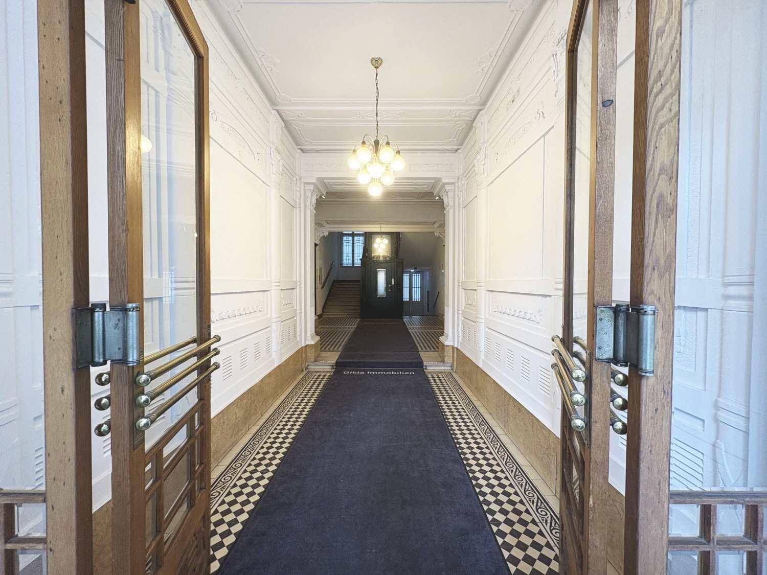 Prunkvoller Eingangsbereich mit hohen Decken, Stuckverzierungen und einem langen Teppich.