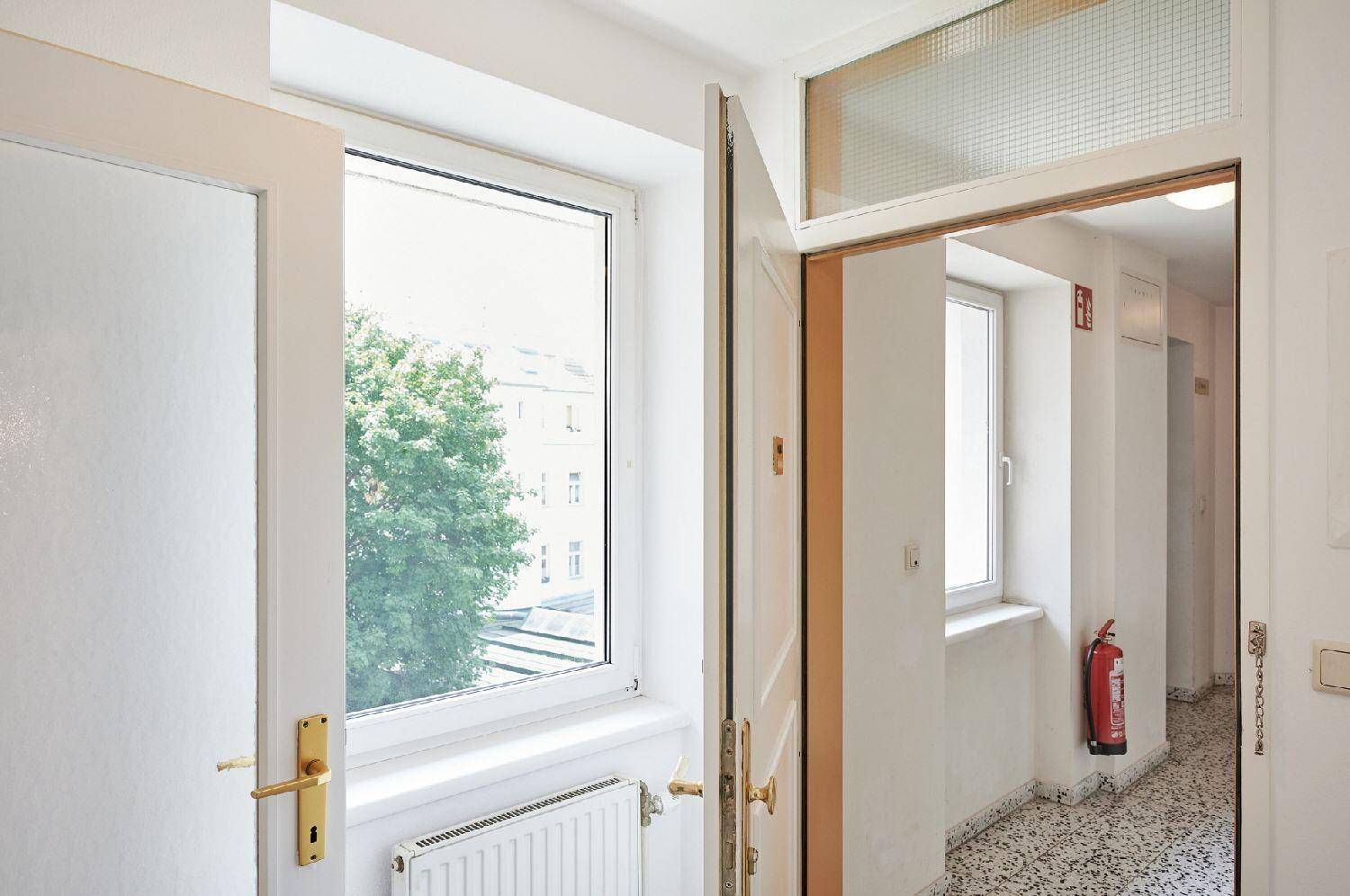 Heller Flur mit Fenster und Blick ins Grüne, ausgestattet mit einem Feuerlöscher.