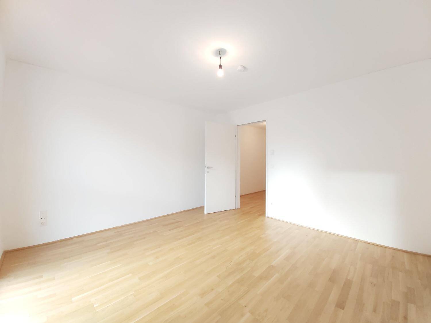 Leeres Zimmer mit hellem Parkettboden und weißen Wänden, bereit zur individuellen Gestaltung.