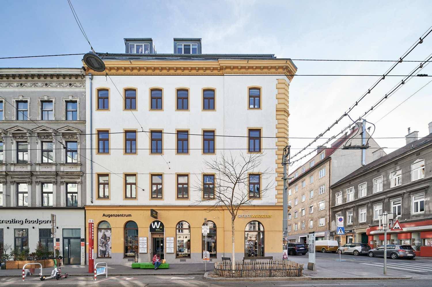 Historische Fassade eines Gebäudes mit vielen Fenstern und Geschäften im Erdgeschoss.