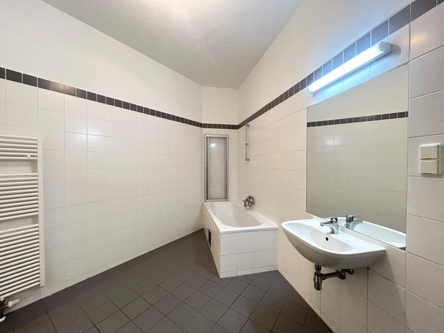 Badezimmer mit Badewanne, Waschbecken, Fliesenboden und beheiztem Handtuchhalter.
