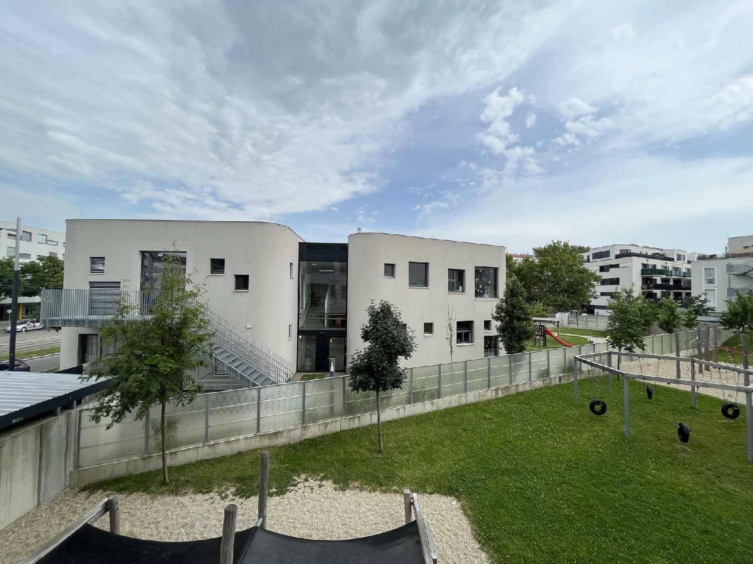 Modernes Wohngebäude mit Spielplatz und Grünflächen unter bewölktem Himmel.