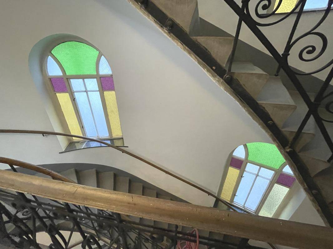 Historisches Treppenhaus mit geschwungenen Stufen und farbenfrohen Buntglasfenstern, die natürliches Licht hereinlassen.