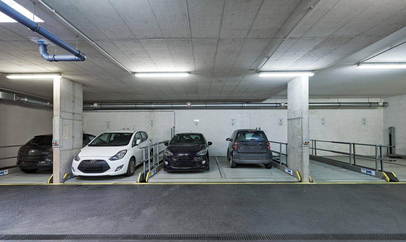 Detailansicht der Parklifts in der Tiefgarage mit geparkten Fahrzeugen und Betonsäulen.