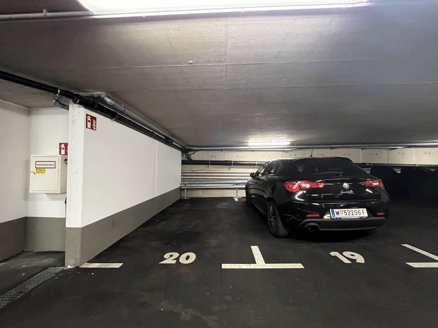 Tiefgaragenstellplatz Nummer 20 mit einem schwarzen Auto und sichtbaren Installationen an der Decke.
