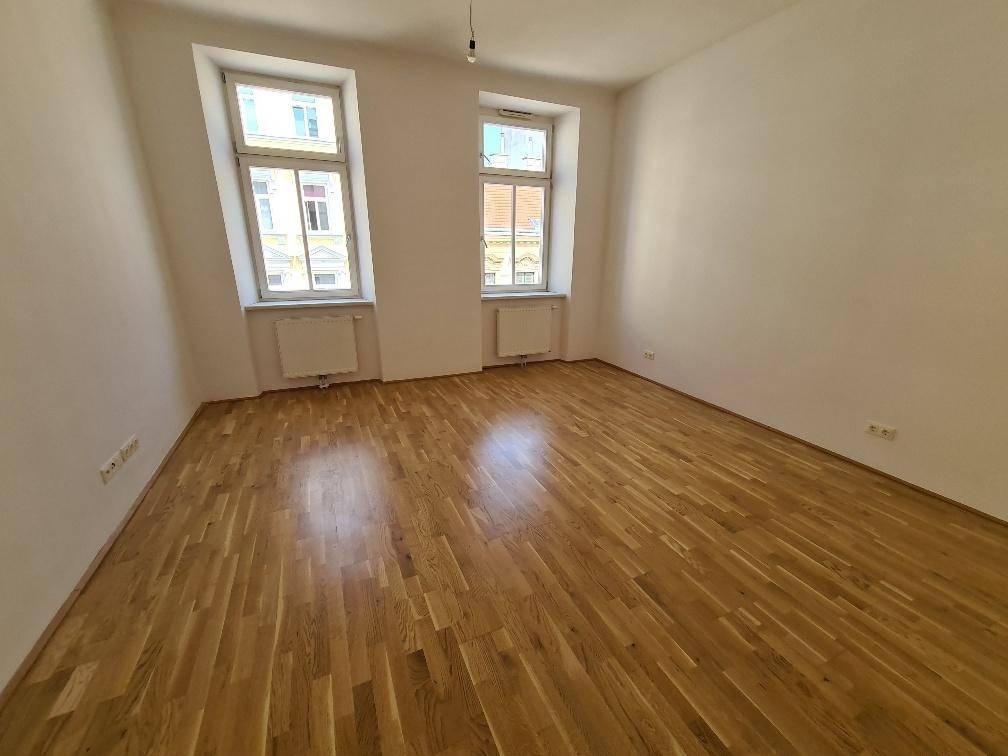 Geräumiger, heller Raum mit Holzboden und zwei Fenstern, ideal als Wohn- oder Schlafzimmer.
