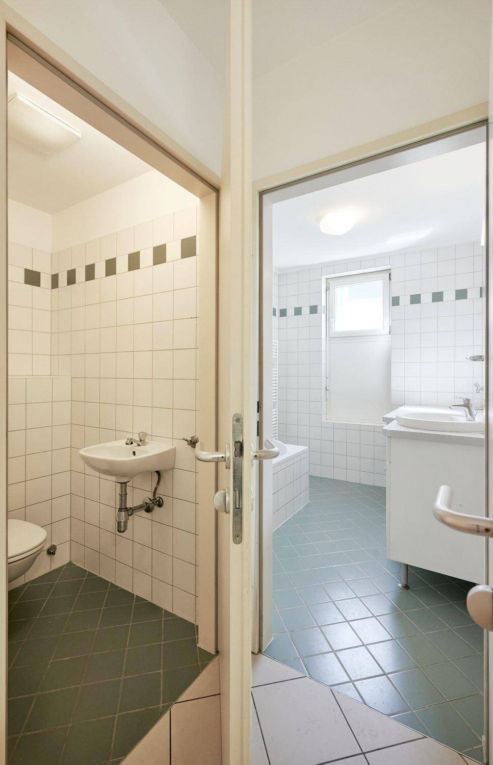 Blick vom Flur in ein Badezimmer und eine separate Toilette, beide mit passenden Fliesen.