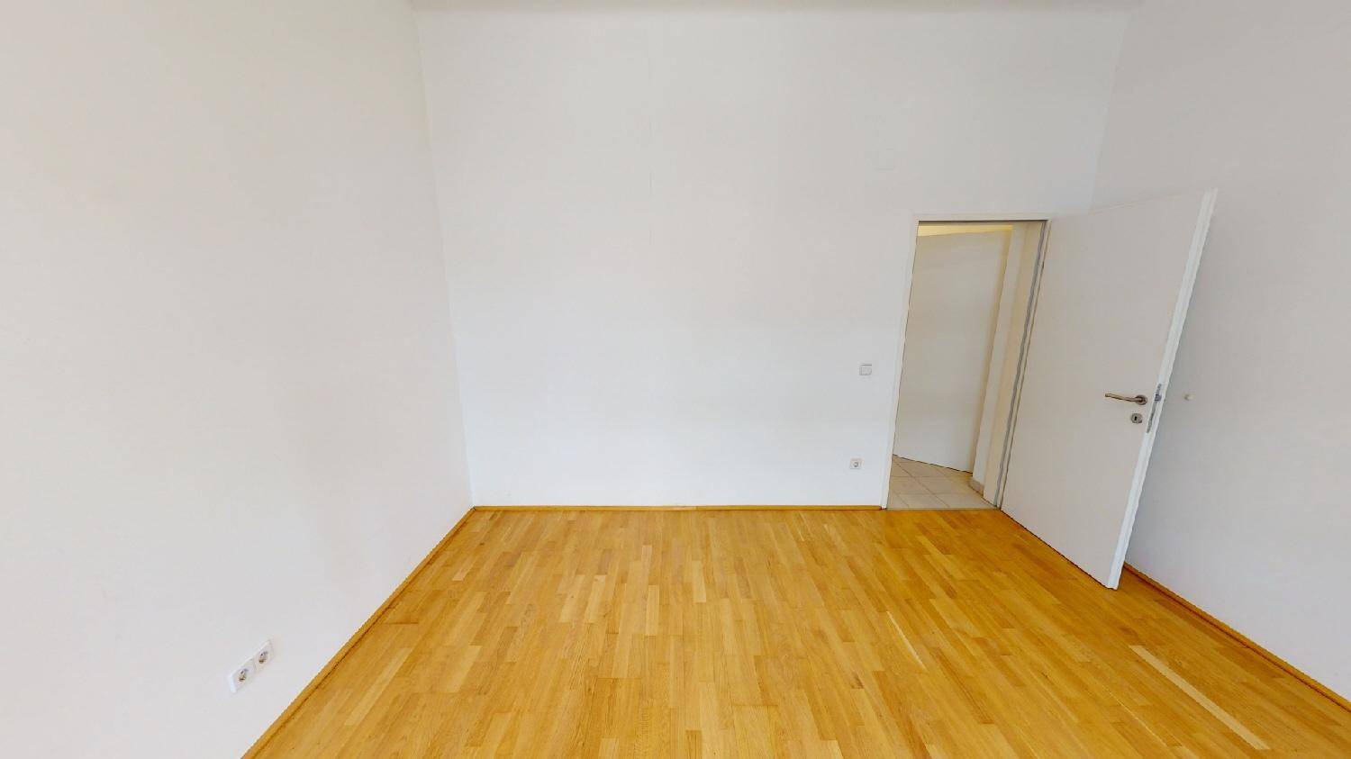 Helles, leeres Zimmer mit Parkettboden und weiß gestrichenen Wänden.