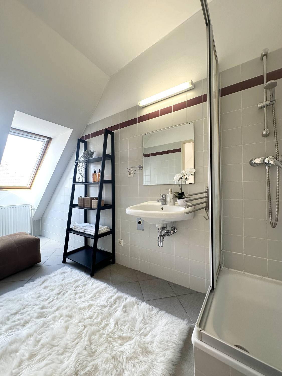 Helles Badezimmer im Dachgeschoss mit Dachfenster, Dusche und modernen Fliesen in Grautönen.
