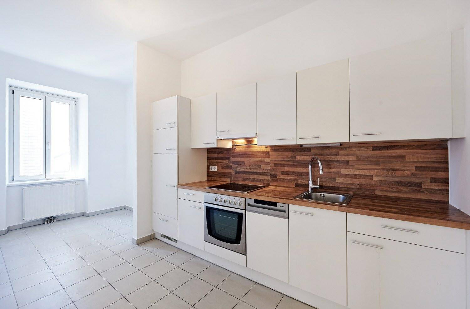 Moderne Einbauküche mit weißen Schränken, Holzoptik-Arbeitsplatte und Fliesenboden.
