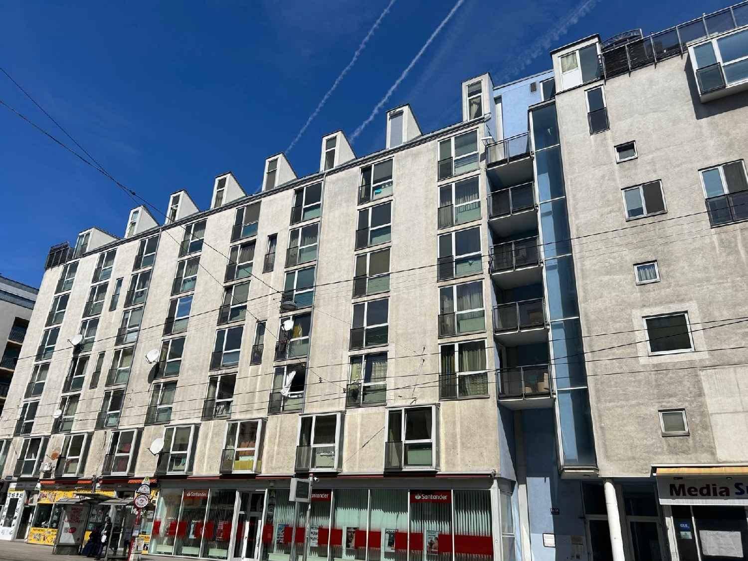 Wohngebäude mit vielen Balkonen und einer hellen Putzfassade unter blauem Himmel.