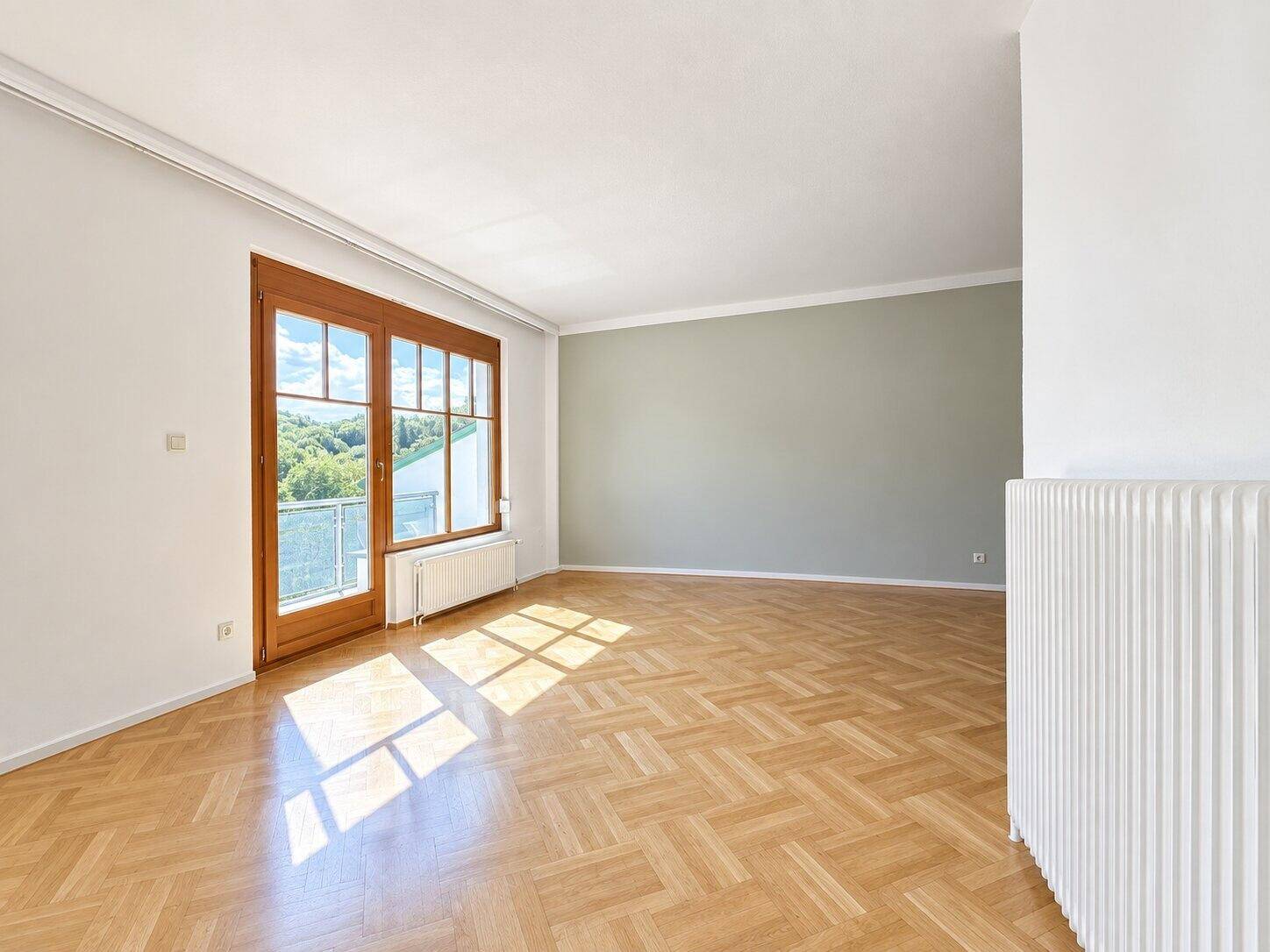 Geräumiges Zimmer mit hellem Fischgrätparkett, großen Fenstern und viel natürlichem Licht.