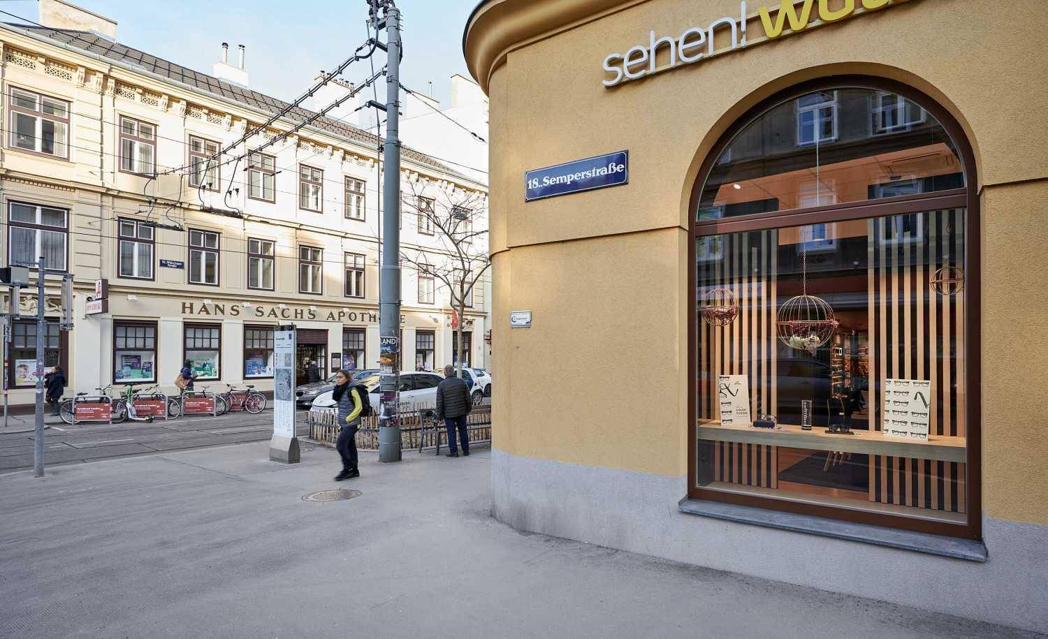 Straßenansicht des Eckgebäudes mit einem Schaufenster und weiteren historischen Gebäuden im Hintergrund.