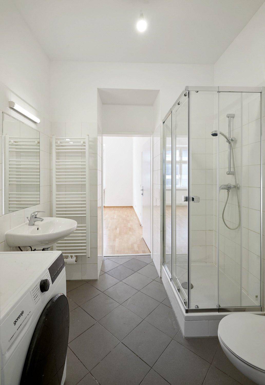 Modernes Badezimmer mit Dusche, Waschbecken, WC und Waschmaschine, ausgestattet mit Fliesenboden.