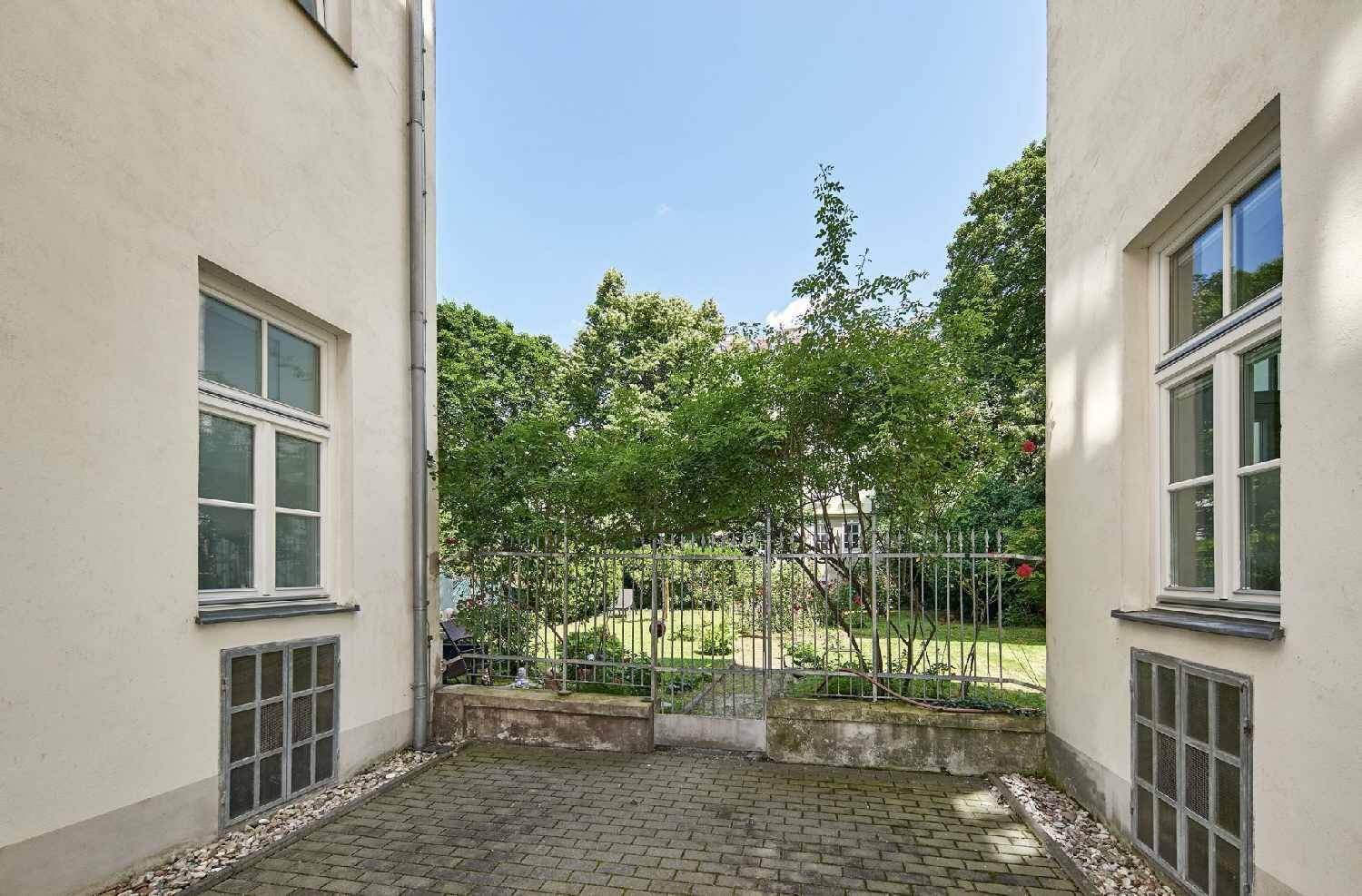 Kleiner gepflasterter Innenhof mit Zugang zu einem grünen Gemeinschaftsgarten mit Bäumen.