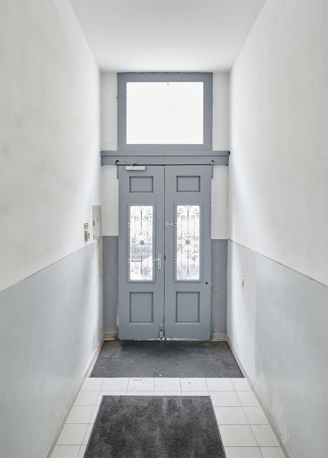 Schmaler Flur mit zweiflügeliger Tür und Oberlicht, der den Eingangsbereich des Gebäudes zeigt.