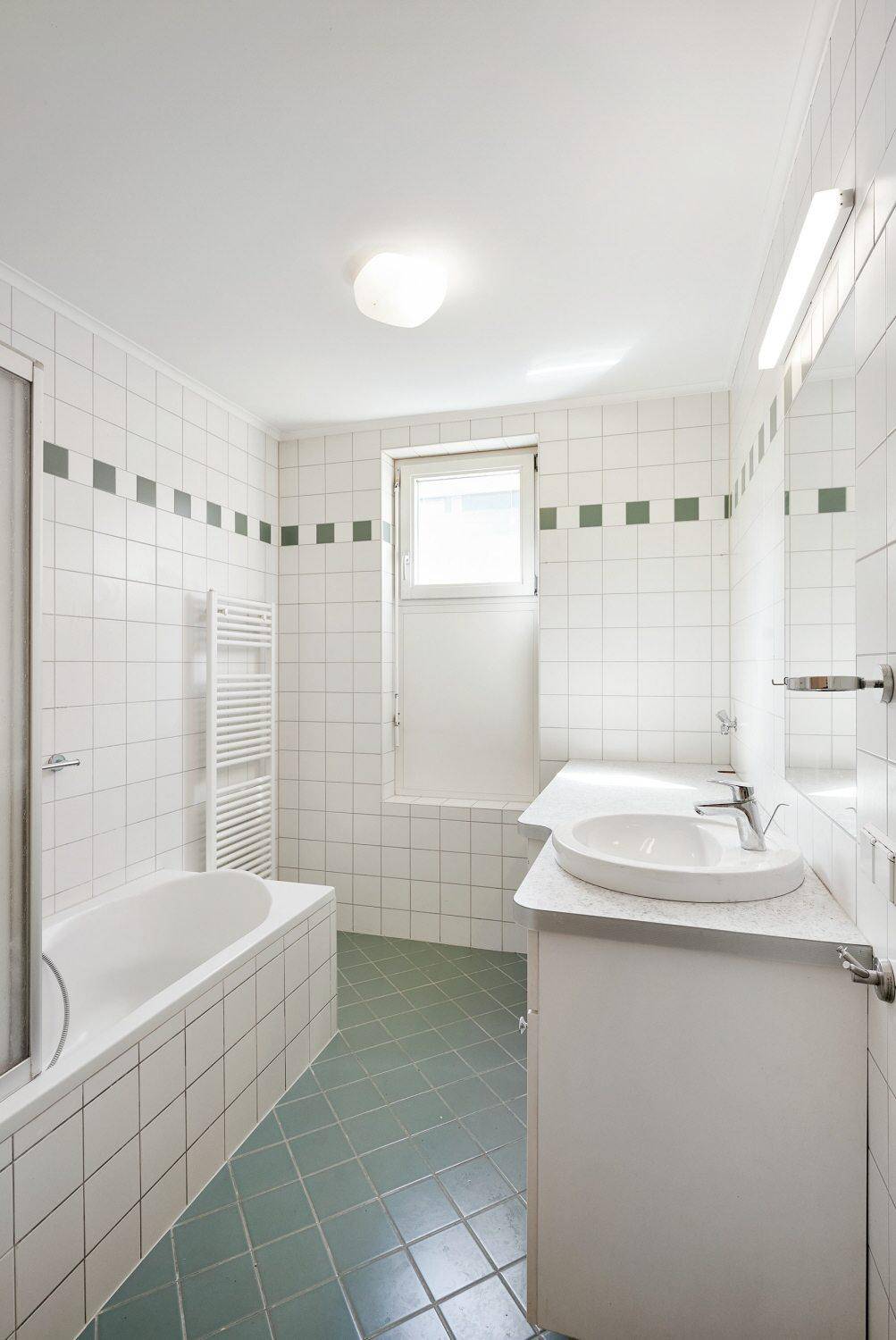 Gefliestes Badezimmer mit Badewanne, Duschabtrennung, Einzelwaschbecken und einem Fenster für Tageslicht.