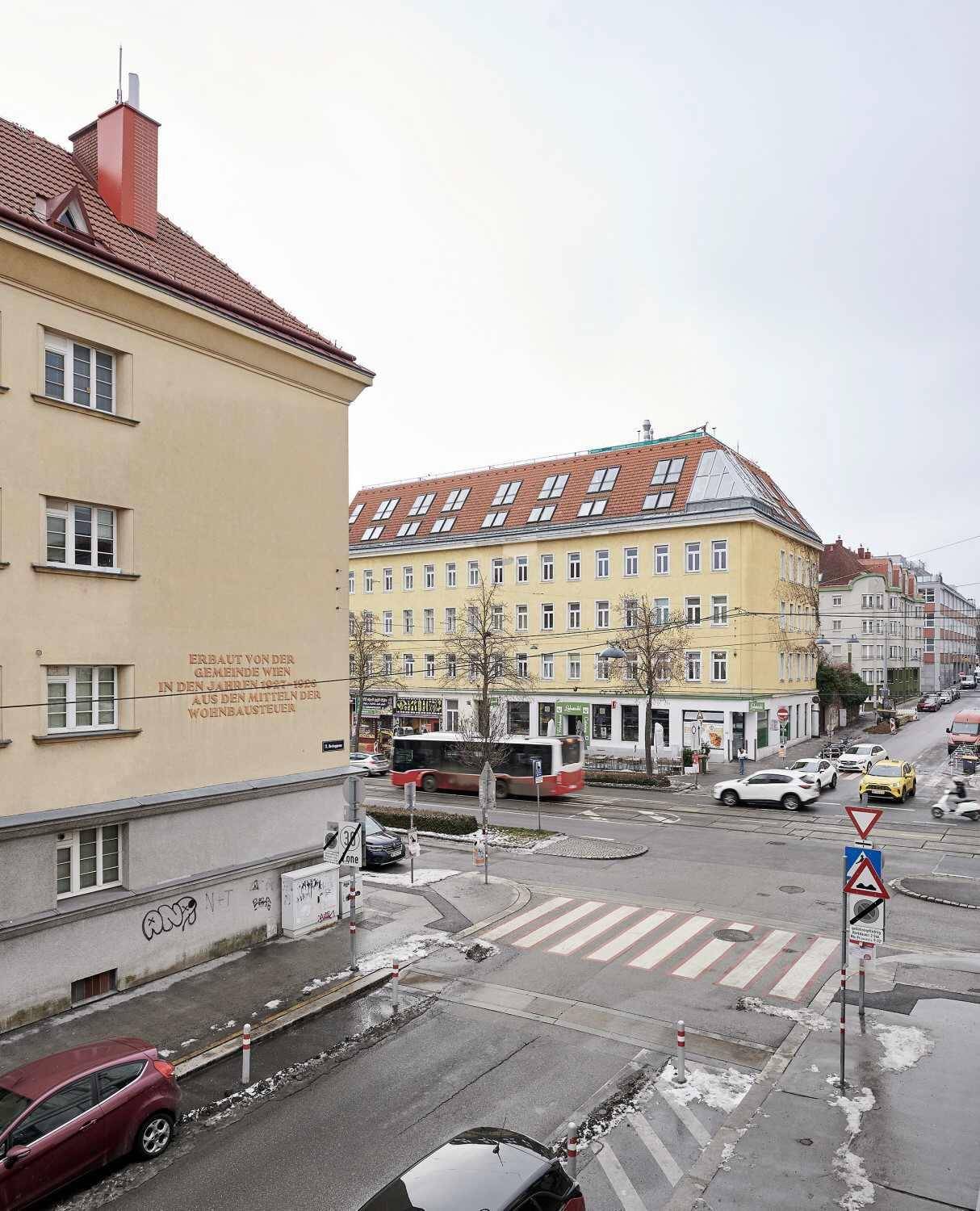 Blick auf eine belebte Stadtstraße mit Gebäuden, Fahrzeugen und Fußgängern an einem Wintertag.