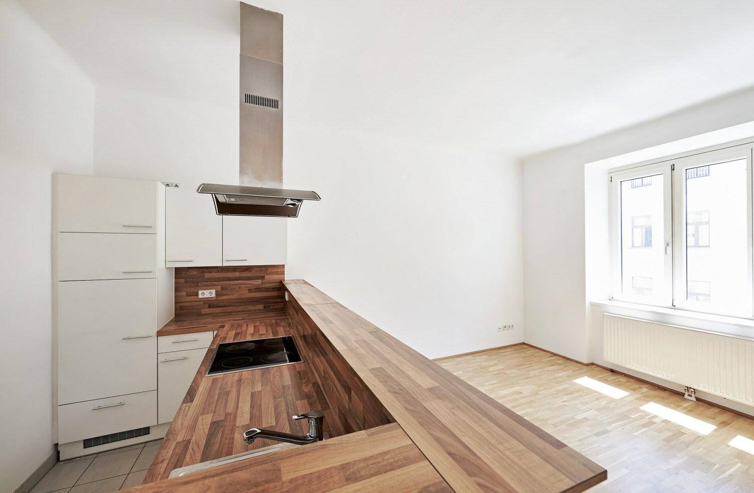 Funktionale Küche mit Holzarbeitsplatte, integrierten Geräten und Fenster für Tageslicht.