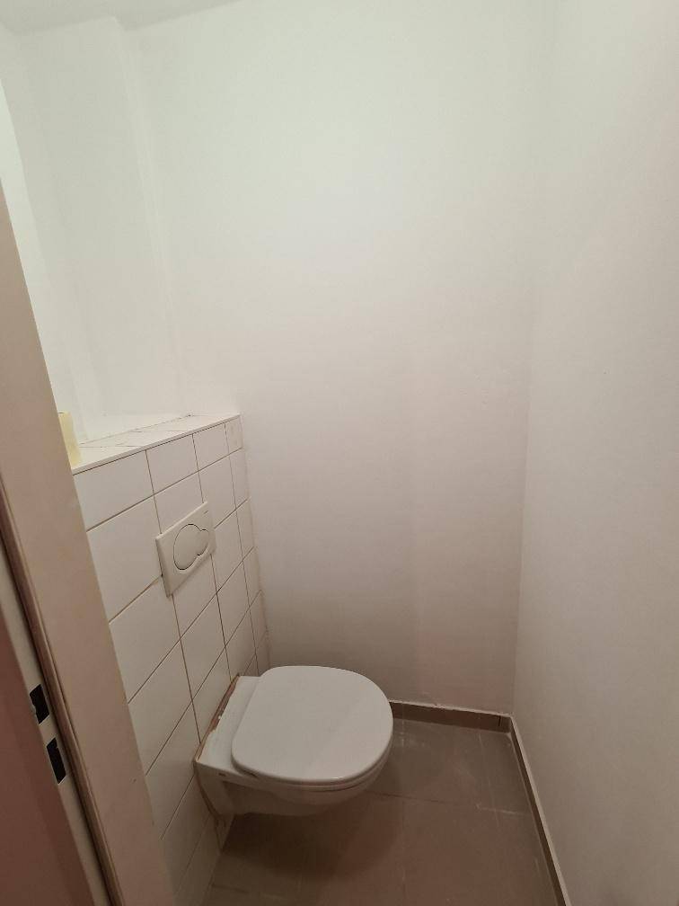 Separate Toilette mit wandhängendem WC und weißen Fliesen an den Wänden.