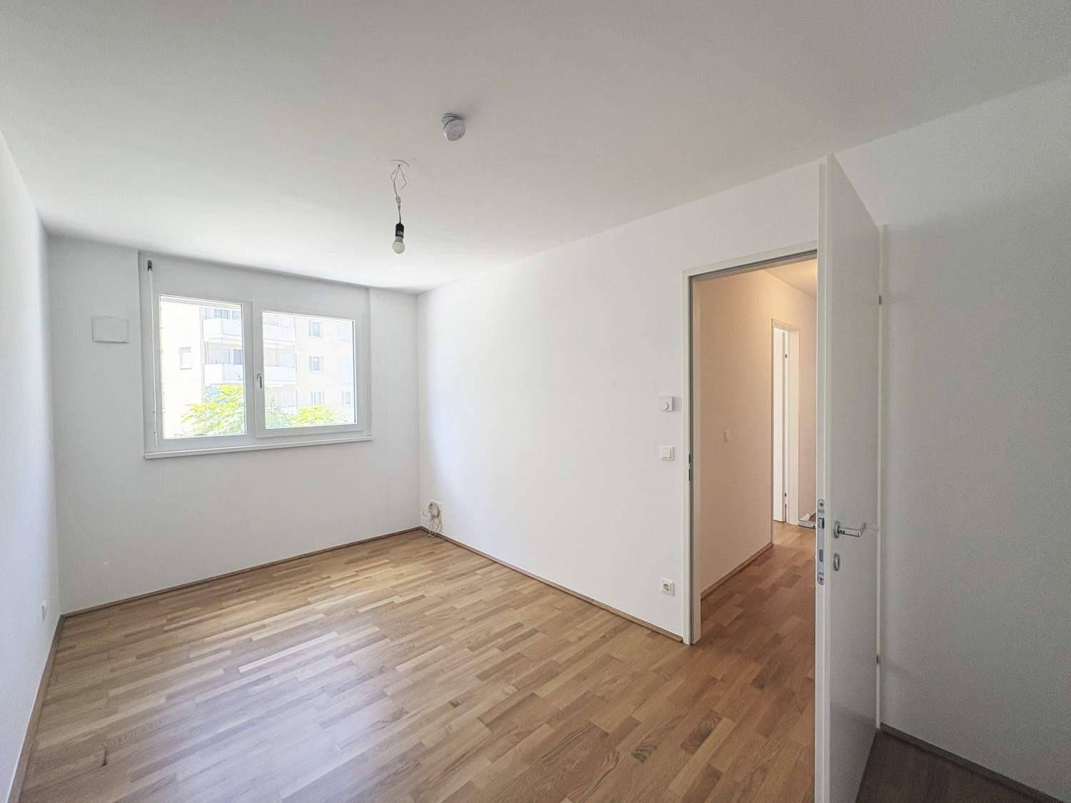 Helles Schlafzimmer mit Holzboden und großem Fenster, bereit zur individuellen Gestaltung.