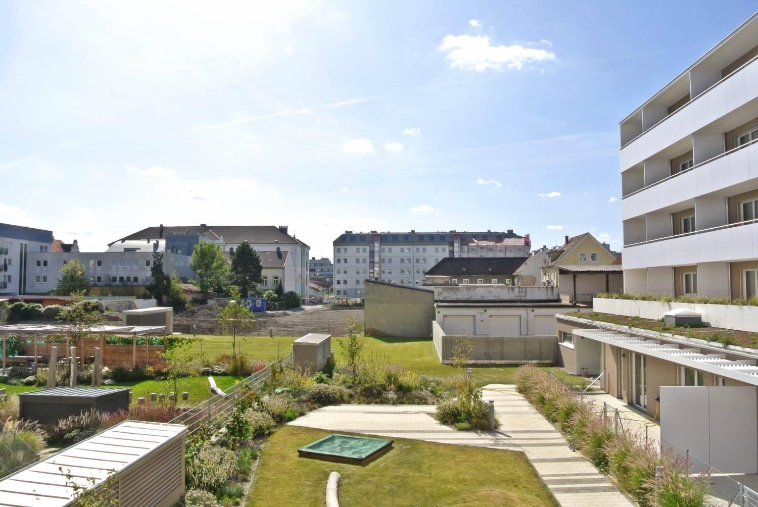 Gepflegte Grünanlage im Innenhof der Wohnanlage mit Wegen und Sitzgelegenheiten unter blauem Himmel.