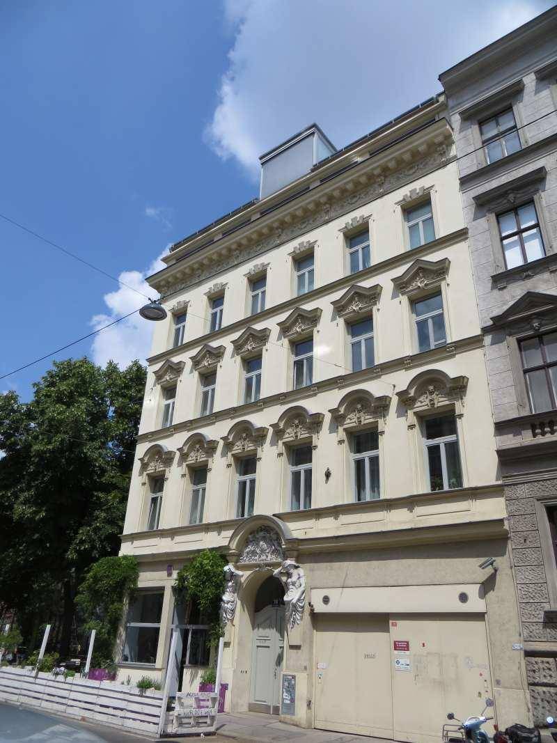 Historische Fassade eines Gebäudes mit aufwendigen Verzierungen und großen Fenstern zur Straße hin.