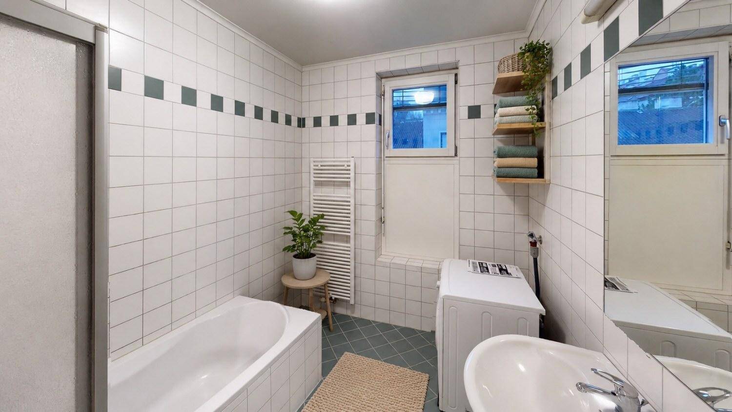 Gefliestes Badezimmer mit Badewanne, Waschbecken, Waschmaschine und Fenster.