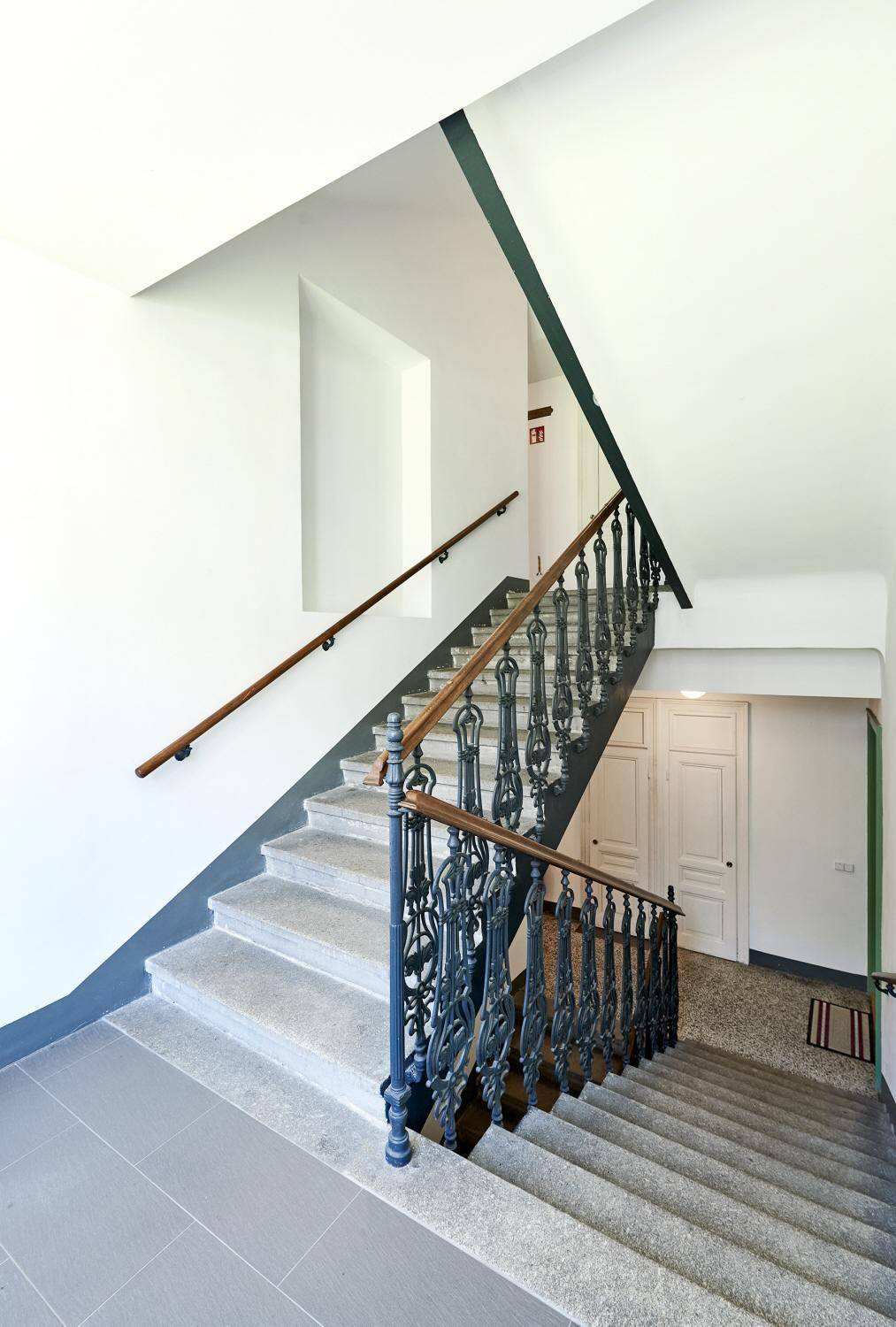 Treppenhaus mit Steinstufen, schmiedeeisernem Geländer und hohen Wänden.