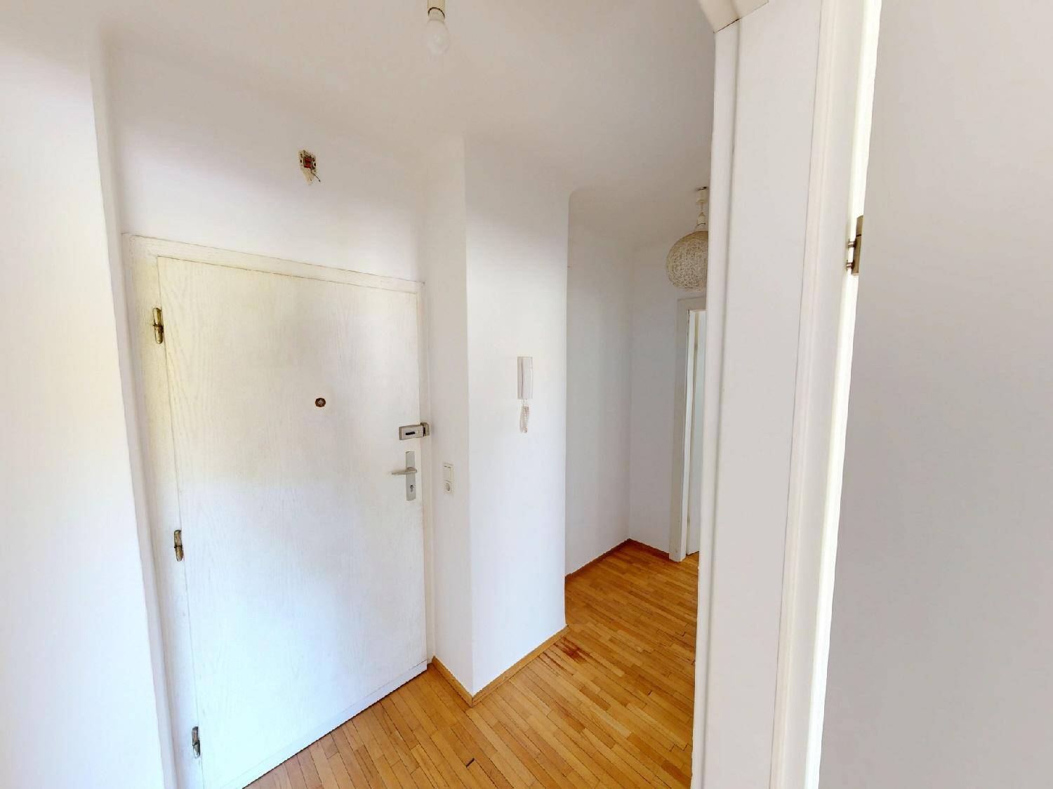 Eingangsbereich mit heller Holztür und Gegensprechanlage, führt in die Wohnung.
