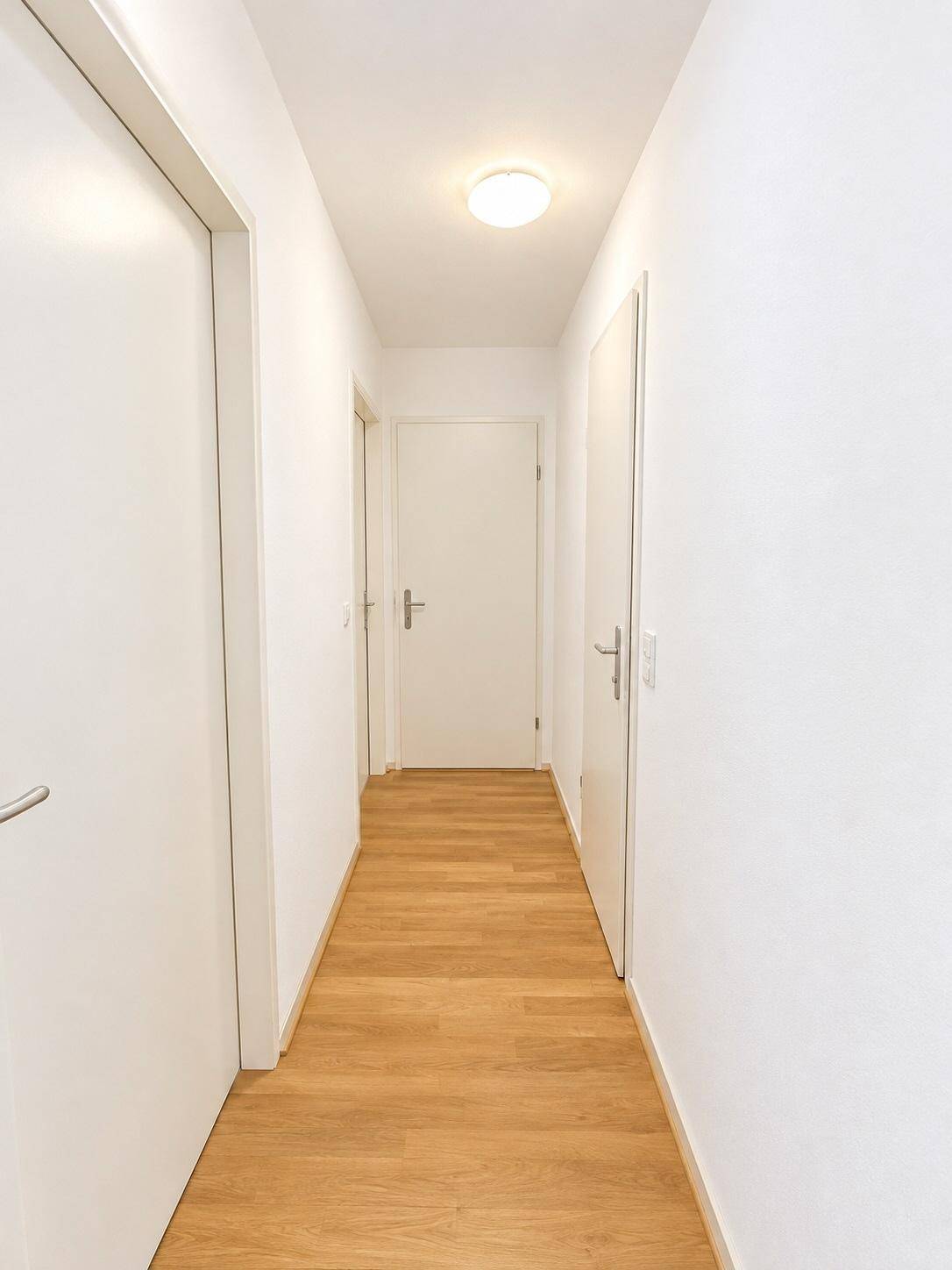 Heller Flur mit Holzboden und mehreren weißen Türen, die zu den Zimmern führen.