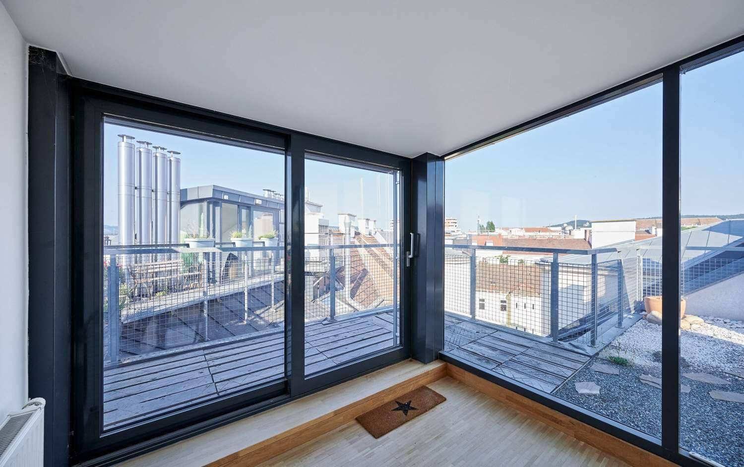Heller Raum mit großen Glasschiebetüren und Zugang zur Dachterrasse mit Stadtblick.