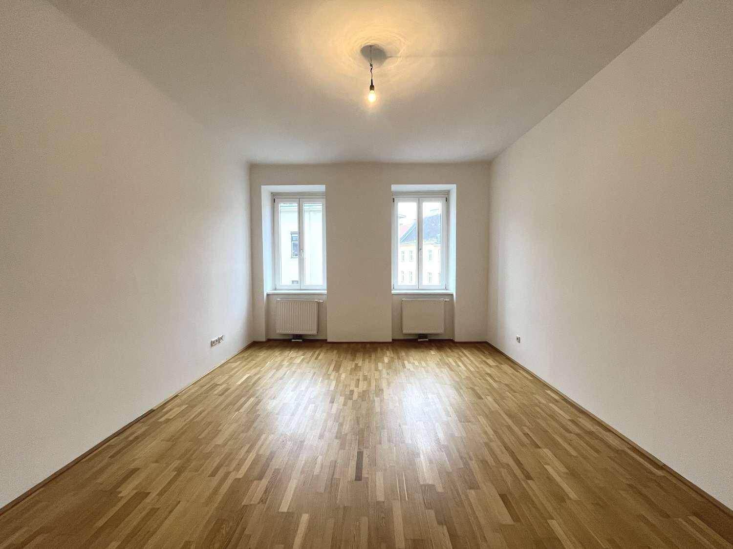 Geräumiges Wohnzimmer mit Parkettboden, zwei Fenstern und viel Tageslicht.