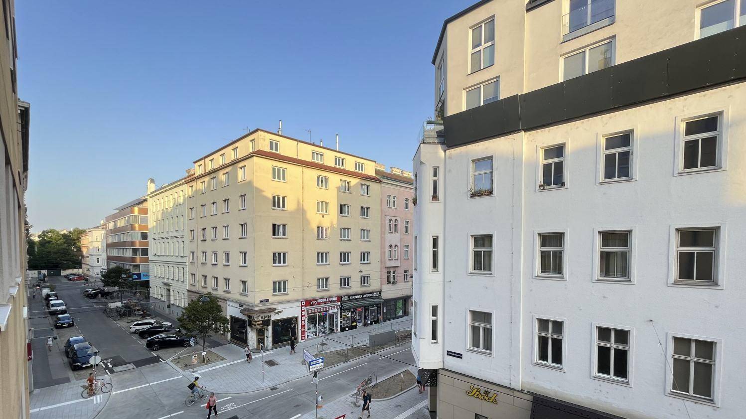 Blick auf eine belebte Stadtstraße mit mehrstöckigen Wohngebäuden unter blauem Himmel.