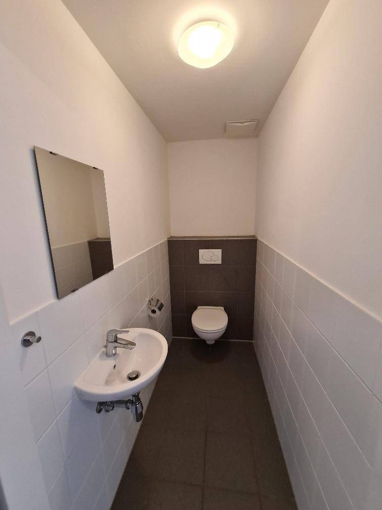 Separates WC mit wandhängender Toilette und kleinem Waschbecken, modern gefliest.