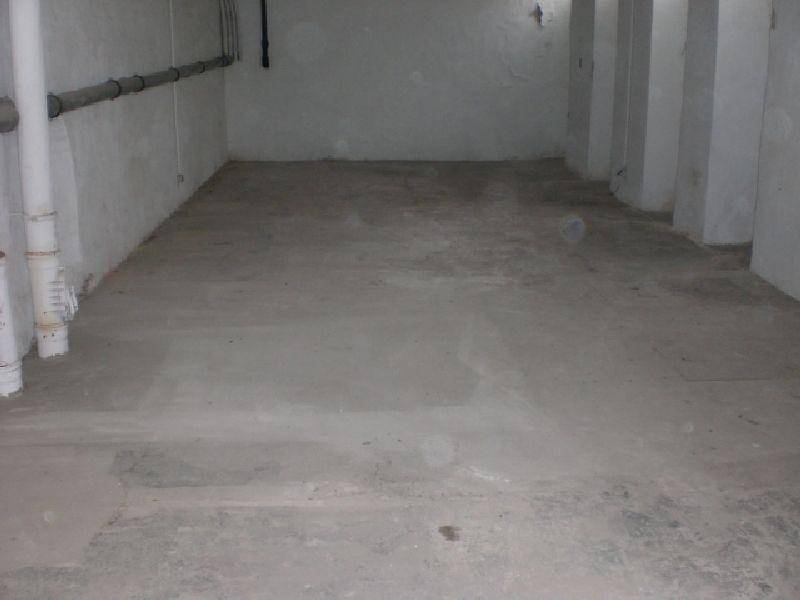 Ein leerer Kellerraum mit Betonboden und sichtbaren Rohren an den Wänden.