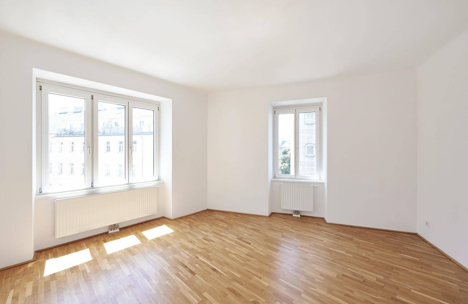 Geräumiges, helles Zimmer mit Holzboden und großen Fenstern, bereit zur individuellen Gestaltung.