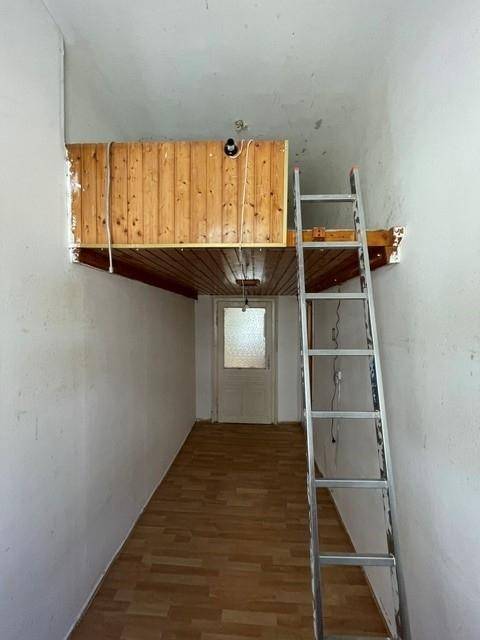 Schmaler Raum mit Holzdecke und Leiter zu einer erhöhten Schlafebene oder Ablagefläche.