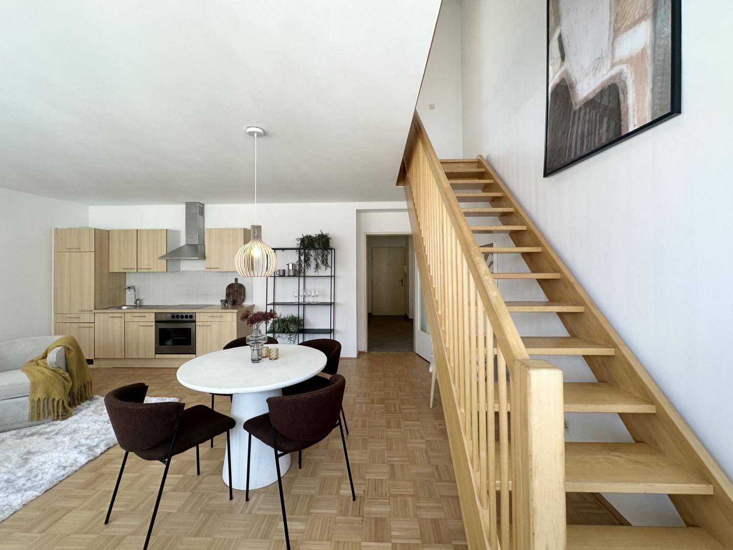 Offener Wohnbereich mit integrierter Küche, Esstisch und heller Holztreppe zum Obergeschoss.