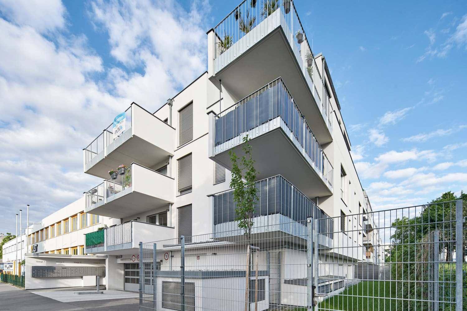 Modernes Mehrfamilienhaus mit mehreren Balkonen und einer Tiefgarage im Vordergrund.