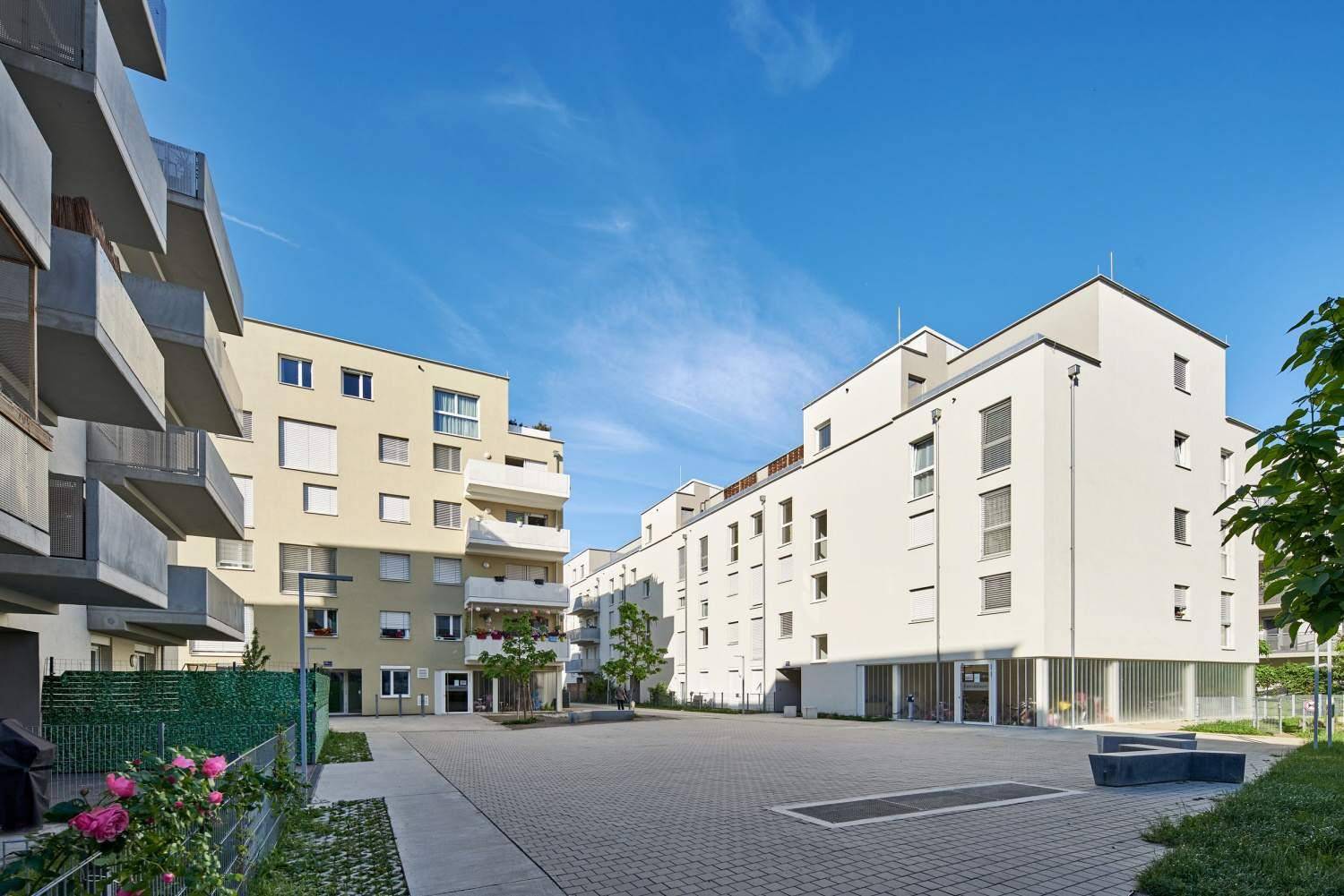 Moderne Wohnanlage mit gepflastertem Innenhof und Bäumen, umgeben von weiteren Wohngebäuden.