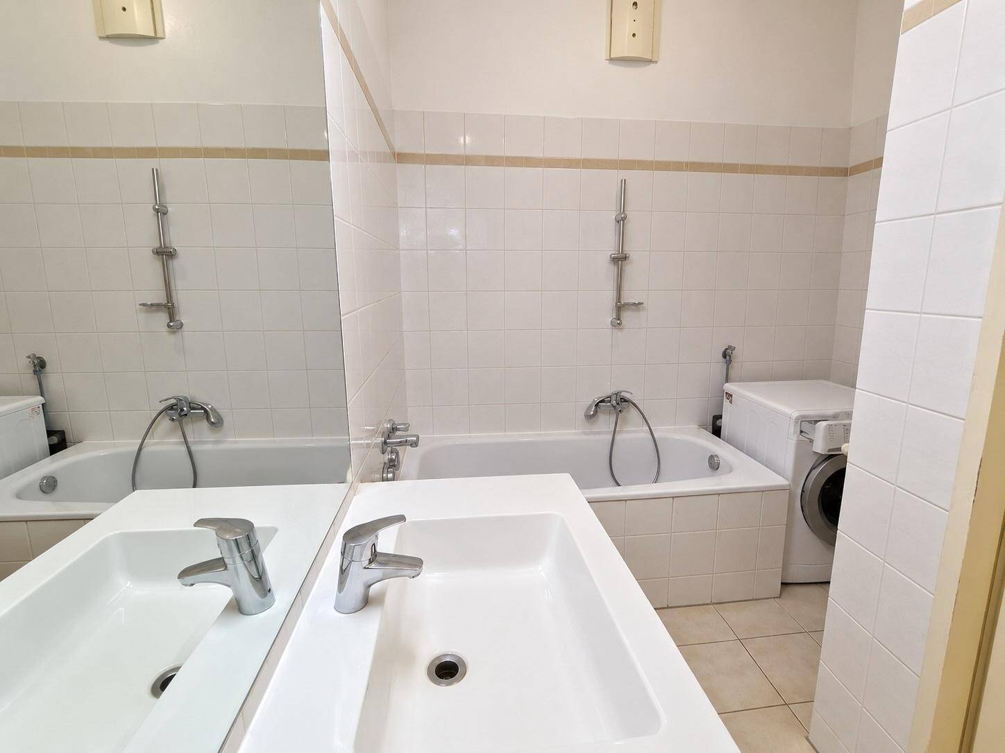 Badezimmer mit Badewanne, Einzelwaschbecken und einer Waschmaschine, gefliest in hellen Tönen.