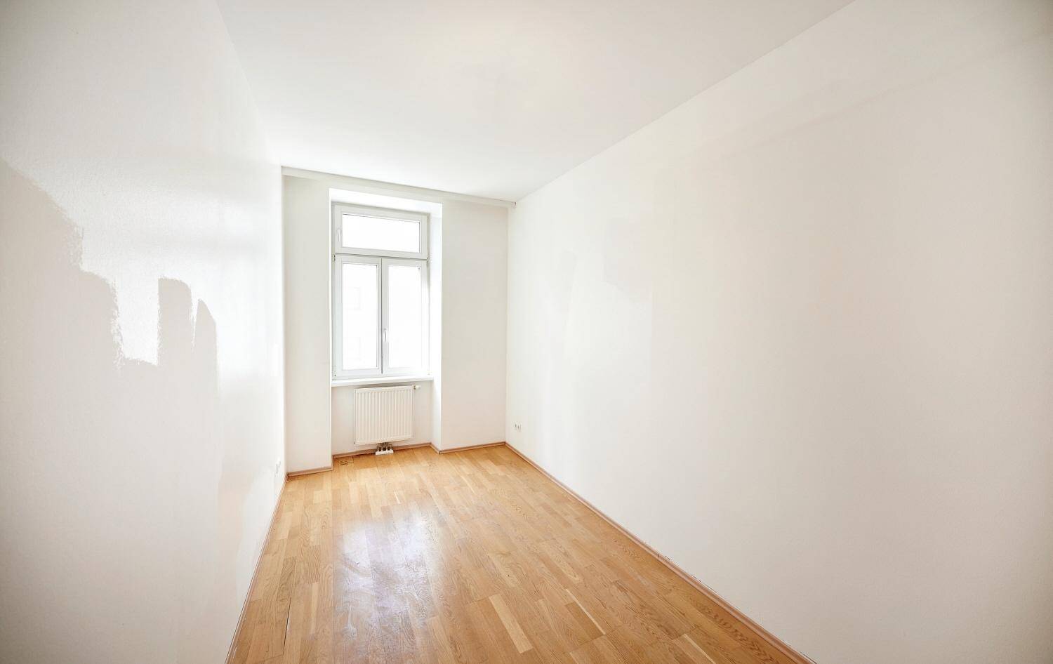 Leeres Zimmer mit Parkettboden und einem Fenster, das für ausreichend Helligkeit sorgt.